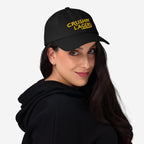 Young woman models the Crushin' Lagers Hat, a black baseball cap with yellow CRUSHIN' LAGERS embroidery, embodying retro style and lager loyalty, perfect for casual brewery visits or relaxed gatherings.