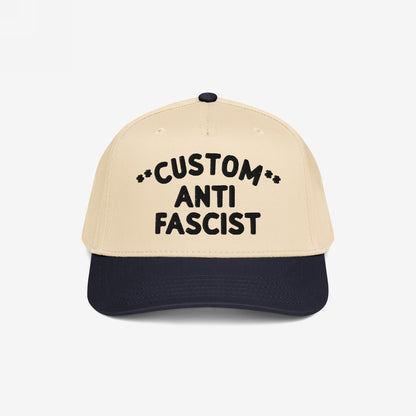Custom Anti-Fascist 5-Panel Hat with light beige crown and navy bill, featuring bold black embroidered text and decorative asterisks. Designed for personalization and activism, it combines style, comfort, and a powerful message.