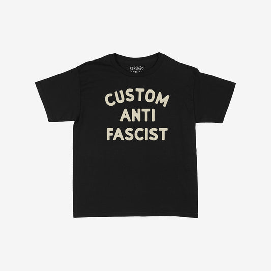 Custom Anti-Fascist Women's Baby Tee features large cream block letters on a black T-shirt, laid flat. The retro design supports equality and anti-fascism, perfect for personalizing with your city or community.