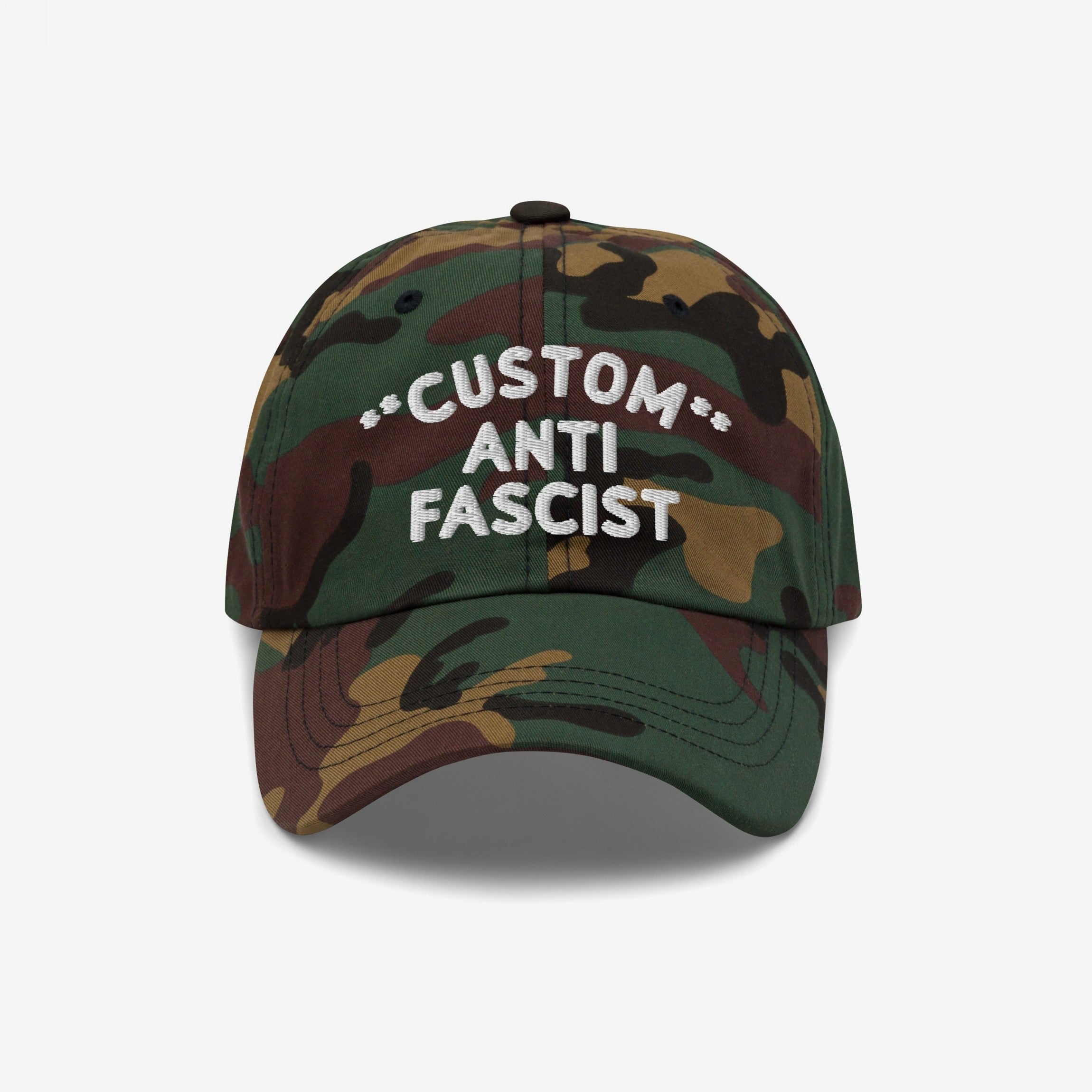 Custom Anti-Fascist Dad Hat with woodland camouflage print features white embroidered text, CUSTOM ANTI FASCIST, on the front. Unstructured, low-profile design, adjustable strap, and pre-curved visor for comfortable, statement-making wear.