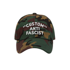 Custom Anti-Fascist Dad Hat with woodland camouflage print features white embroidered text, CUSTOM ANTI FASCIST, on the front