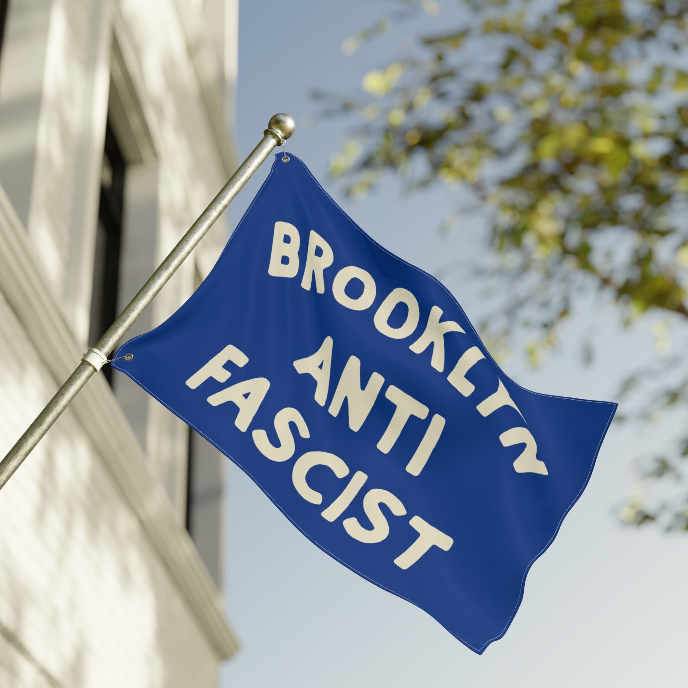 The Custom Anti-Fascist Flag displays BROOKLYN ANTI FASCIST in bold cream letters on a blue background, mounted on a building, symbolizing unity against fascism and hate.