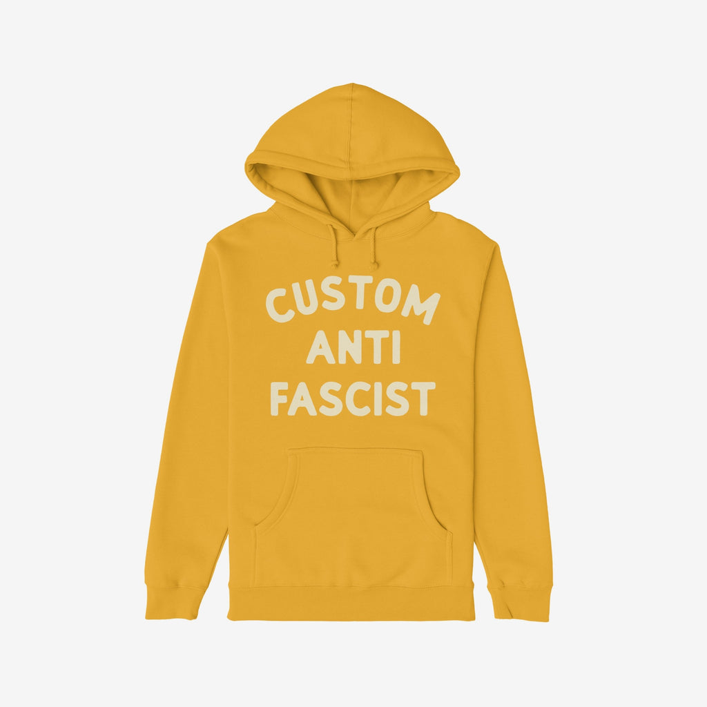 Custom Anti-Fascist Hoodie featuring bold white lettering on mustard-yellow fabric with a kangaroo pocket and drawstring hood, embodying activism and comfort for those standing against fascism.