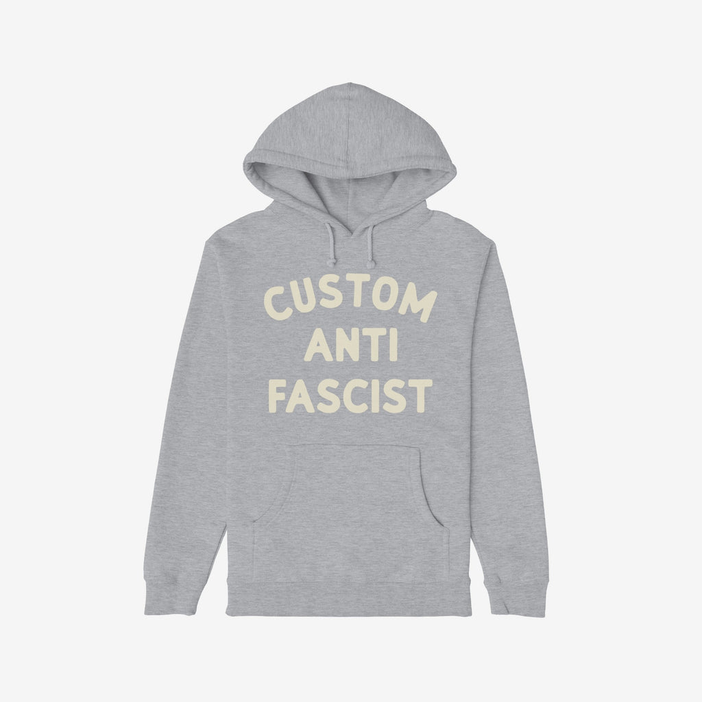 Custom Anti-Fascist Hoodie featuring bold cream text on a light-gray pullover with front kangaroo pocket, designed for personalization and active expression of values against fascism, adding comfort and activism to your wardrobe.