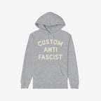 Custom Anti-Fascist Hoodie featuring bold cream text on a light-gray pullover with front kangaroo pocket, designed for personalization and active expression of values against fascism, adding comfort and activism to your wardrobe.