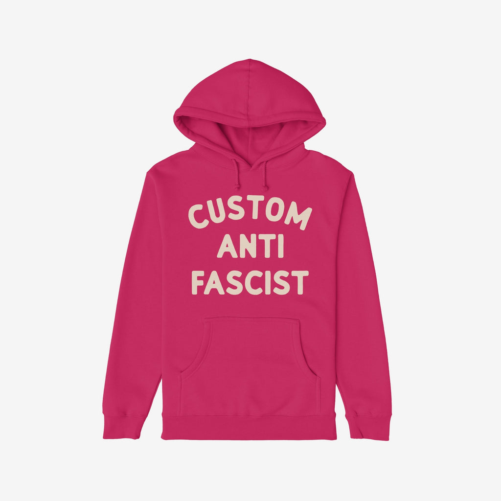 The Custom Anti-Fascist Hoodie features cream block lettering on a deep pink/magenta pullover, promoting activism and personalization. Includes a kangaroo pocket and drawstring hood for comfort and style.