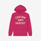 The Custom Anti-Fascist Hoodie features cream block lettering on a deep pink/magenta pullover, promoting activism and personalization. Includes a kangaroo pocket and drawstring hood for comfort and style.