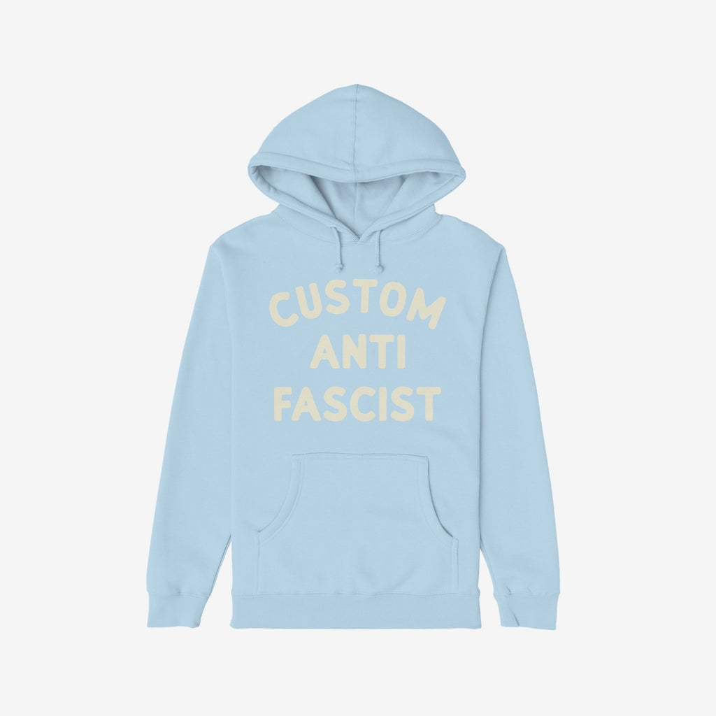 Custom Anti-Fascist Hoodie with front kangaroo pocket features CUSTOM ANTI FASCIST in cream. Ideal for activists, this light-blue pullover is designed for warmth and statement-making.