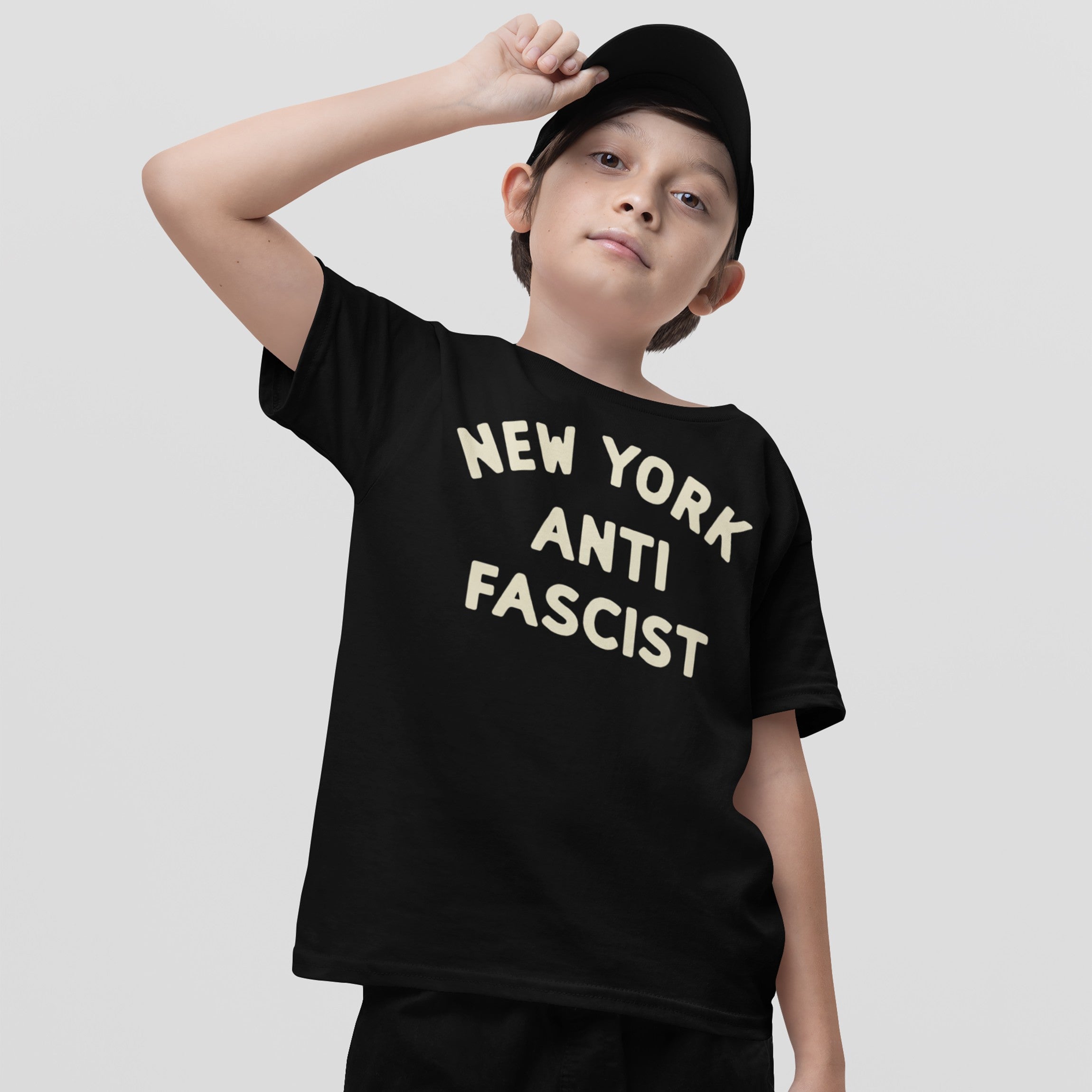Custom Anti-Fascist Kids T-shirt: A young boy wears a black cap and loose-fit black tee with NEW YORK ANTI FASCIST in off-white, symbolizing empowerment and activism for young voices.