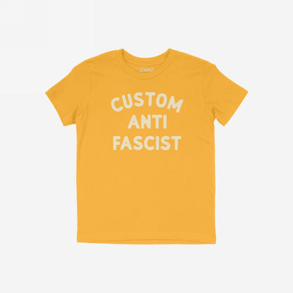 Mustard-yellow Custom Anti-Fascist Kids T-shirt featuring off-white text across the chest. The phrase can be personalized for young activists, showcasing a commitment to anti-fascist values. Brand label visible inside neckline.