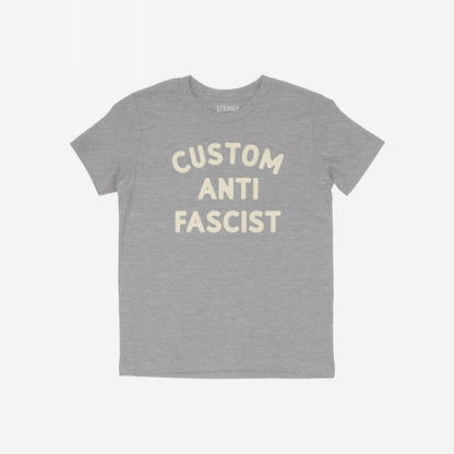 Custom Anti-Fascist Kids T-shirt featuring bold, off-white block letters on a heather-gray tee. The shirt has a crew neckline, short sleeves, and a small STRANGE. label at the collar.