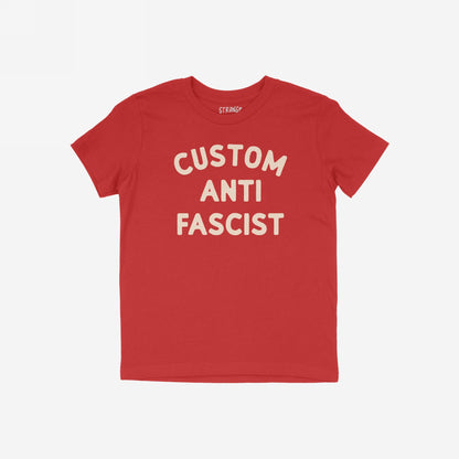 Custom Anti-Fascist Kids T-shirt featuring bold, off-white CUSTOM ANTI FASCIST text on a red short-sleeve. Ideal for young activists, this tee combines comfort with a powerful message.