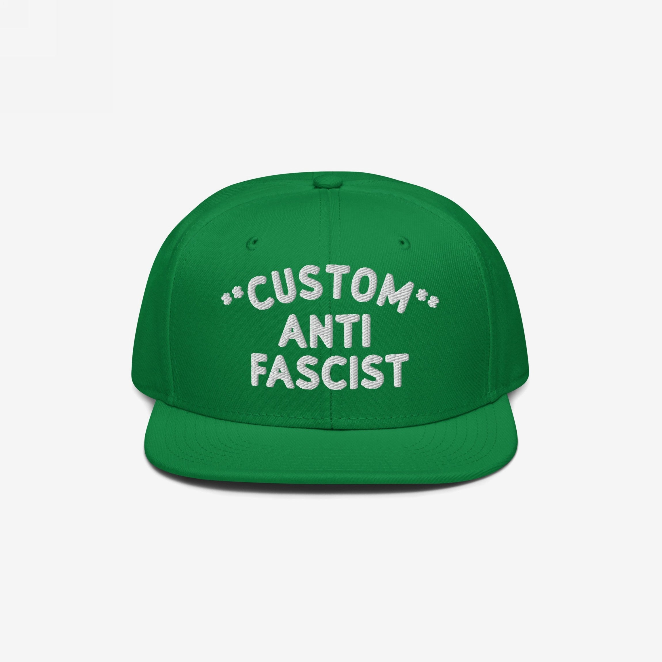 Green flat-bill cap with CUSTOM ANTI FASCIST embroidered in white. The Custom Anti-Fascist Snapback Hat offers personalization options, adjustable fit, and showcases your stance against fascism.