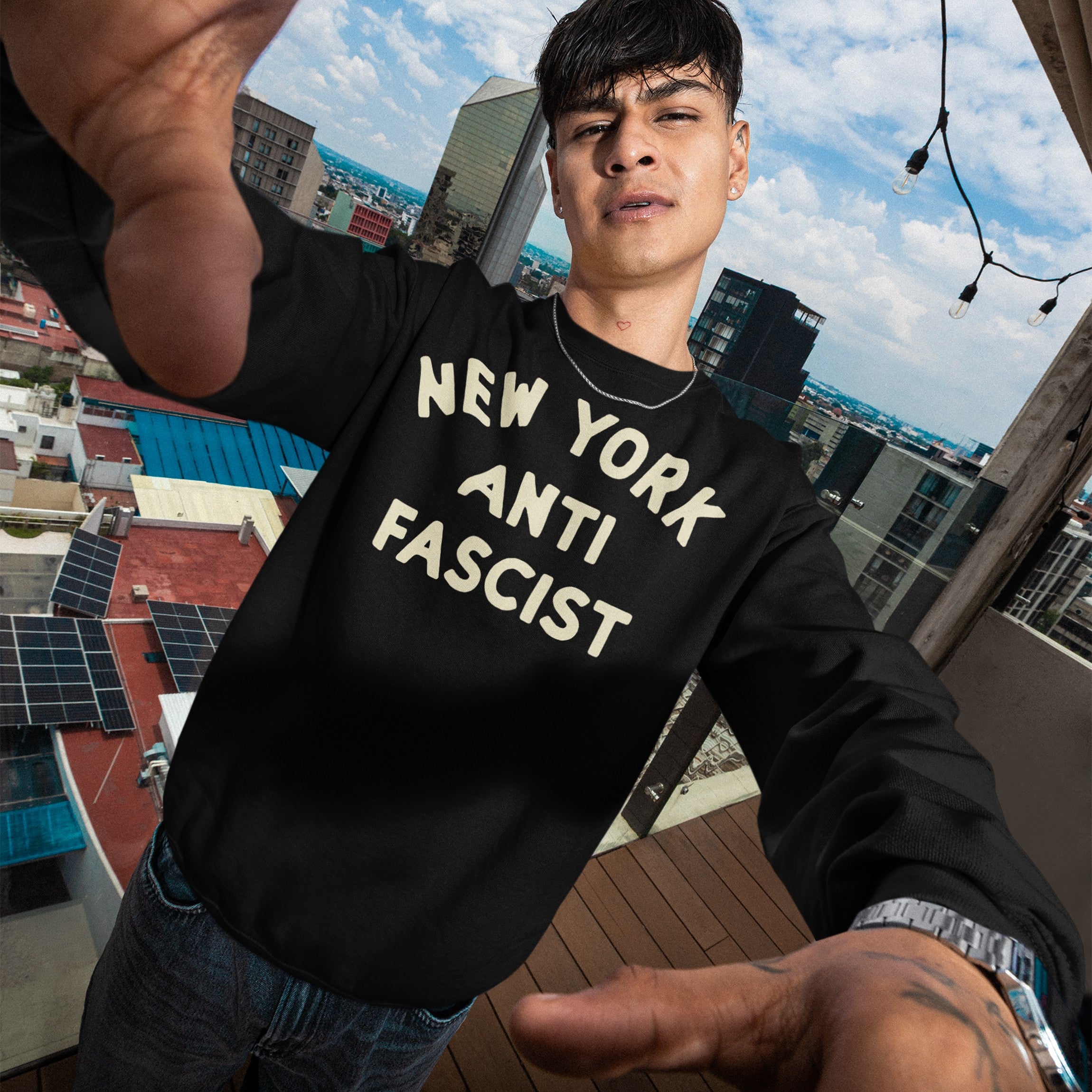 Young man on rooftop wearing a Custom Anti-Fascist Sweatshirt with bold cream text, NEW YORK ANTI FASCIST, embodying activism and style.