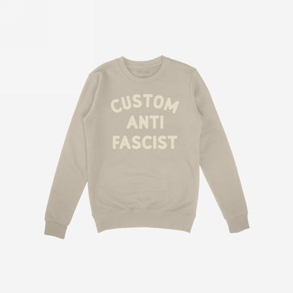 Custom Anti-Fascist Sweatshirt featuring bold off-white block letters on a light-beige crewneck. Personalize the Custom text to express your values and make a statement against fascism.