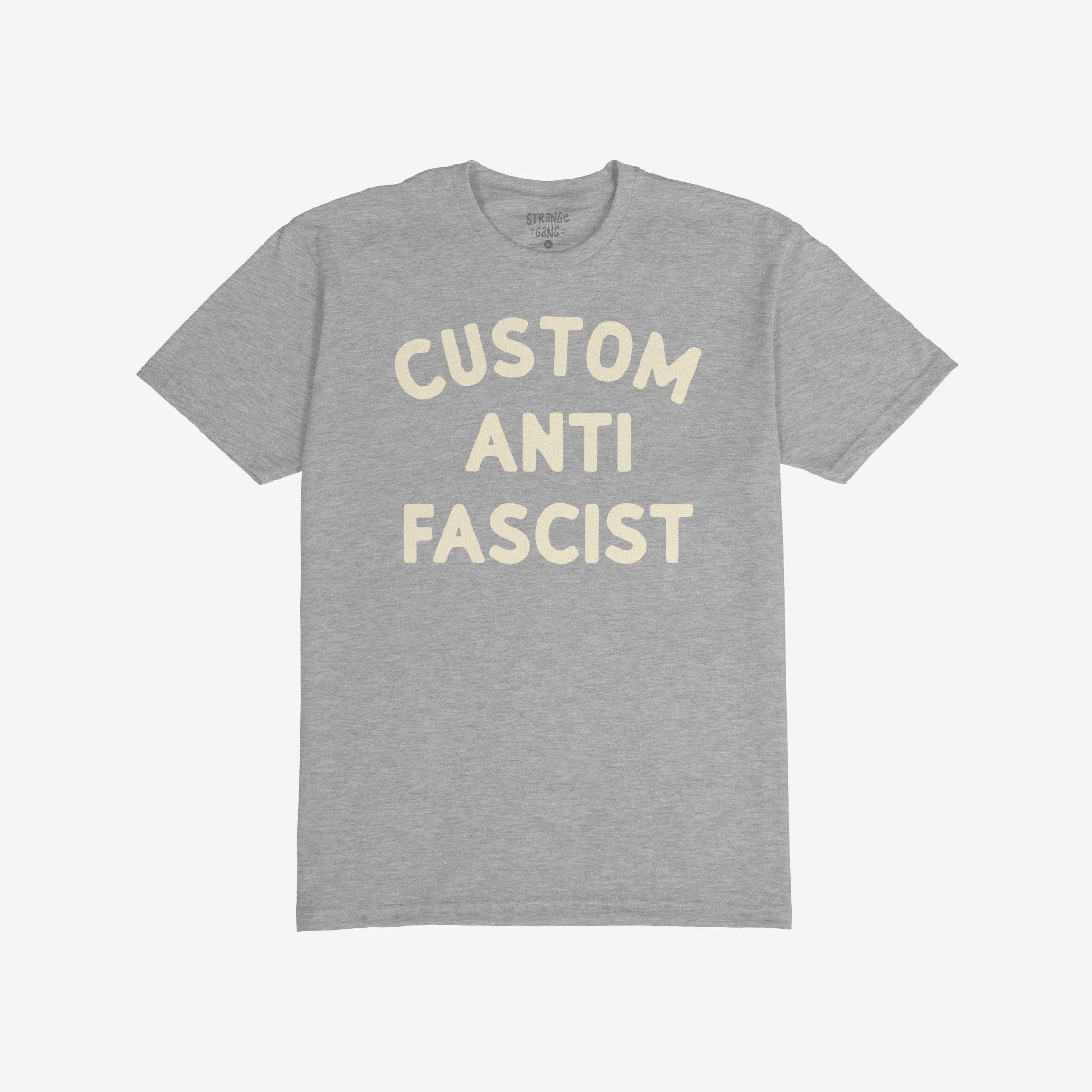 Heather-gray T-shirt with “CUSTOM ANTI FASCIST” in off-white letters, showcasing a strong statement. The neck label reads “STRANGE GANG.” Ideal for expressing anti-fascist views and personalizing activism.