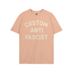 Light blue Custom Anti-Fascist T-shirt with cream block letters reading “CUSTOM ANTI FASCIST” across the front, embodying