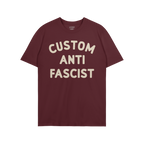 Custom Anti-Fascist T-shirt featuring bold cream text CUSTOM ANTI FASCIST on a maroon crew-neck, embodying a strong anti-fasc