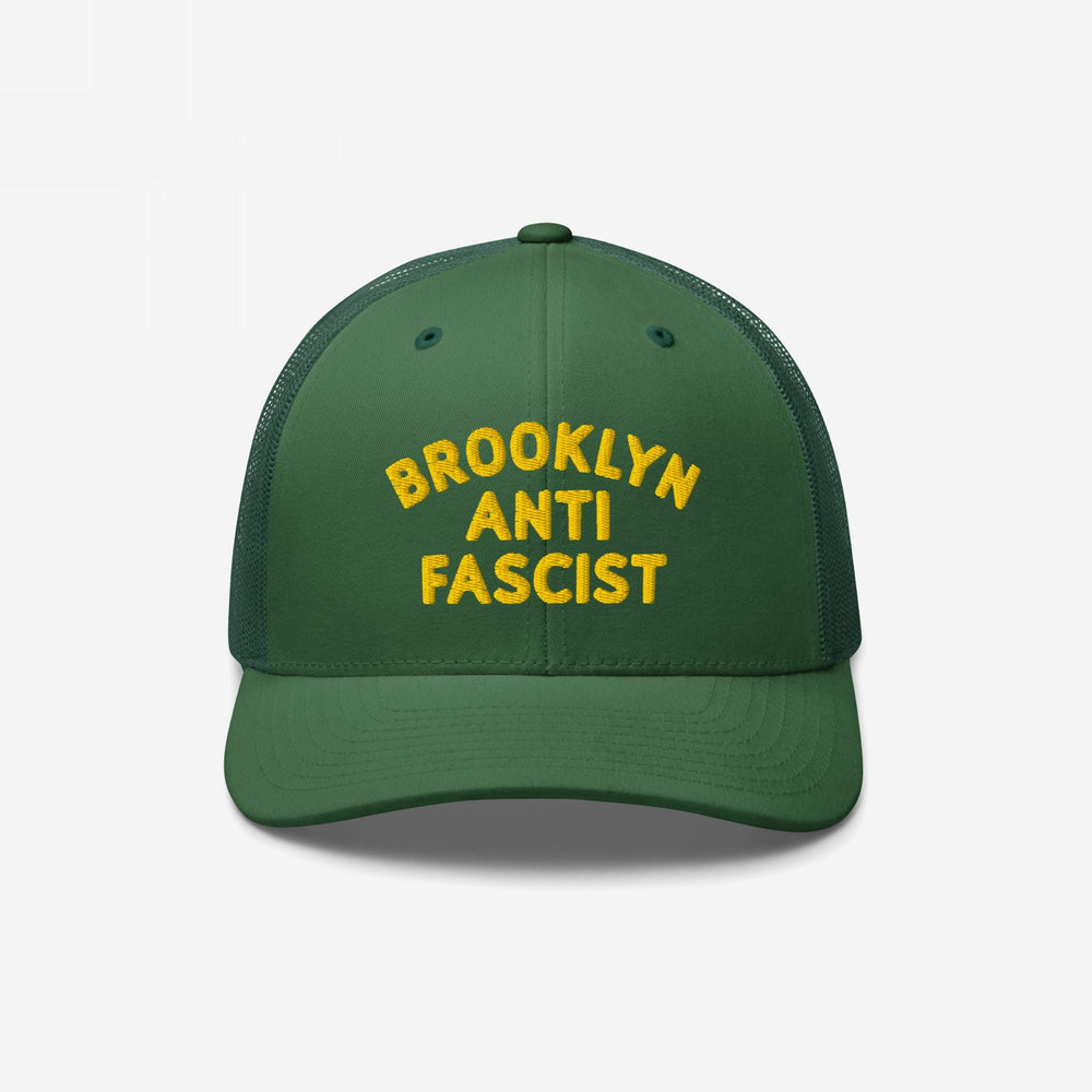 Custom Anti-Fascist Trucker Hat featuring bold yellow BROOKLYN ANTI FASCIST embroidery on the front. Green design with breathable mesh back and adjustable snap closure, embodying a message of resistance and equality.