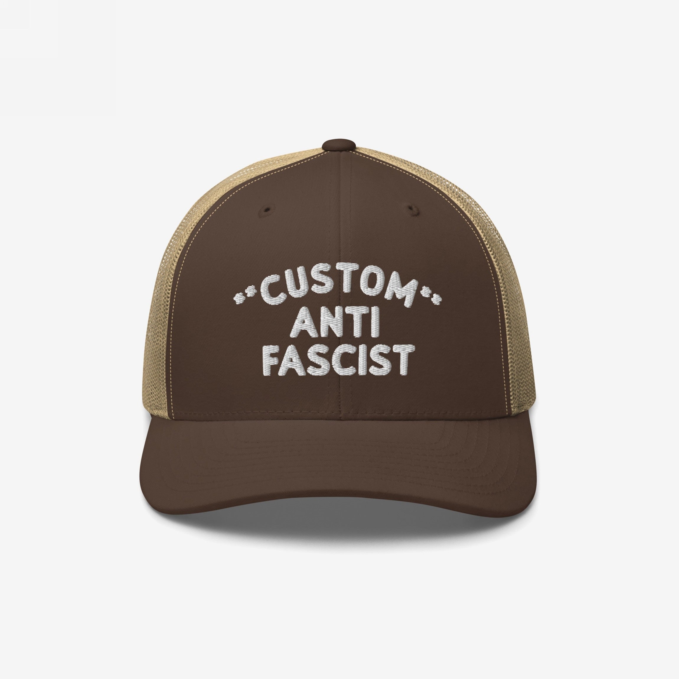 Brown-and-tan trucker cap with mesh back, featuring white embroidered CUSTOM ANTI FASCIST text, highlighting personalizable design. Emphasizes anti-fascist message with adjustable snap closure, promoting equality and individuality.