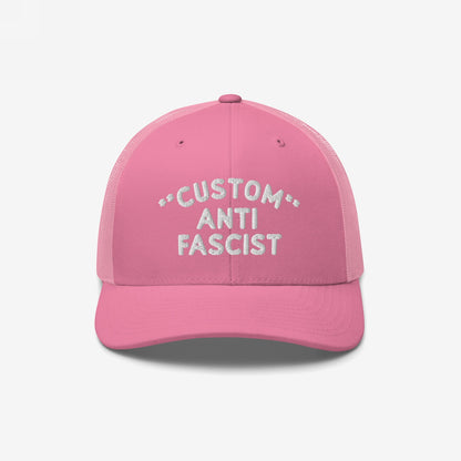 Custom Anti-Fascist Trucker Hat features a pink design with white CUSTOM ANTI FASCIST embroidery. The hat includes mesh panels and an adjustable snapback, conveying a bold anti-fascist message.