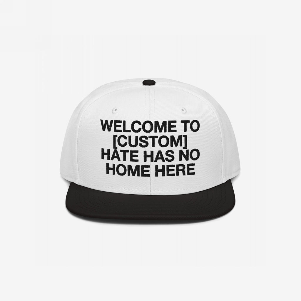 Custom Hate Has No Home Here Snapback Hat with a white crown and black brim, featuring bold black text for personalizing your city name. Embroidered EGOPROOF logo on the back, emphasizing unity and justice.