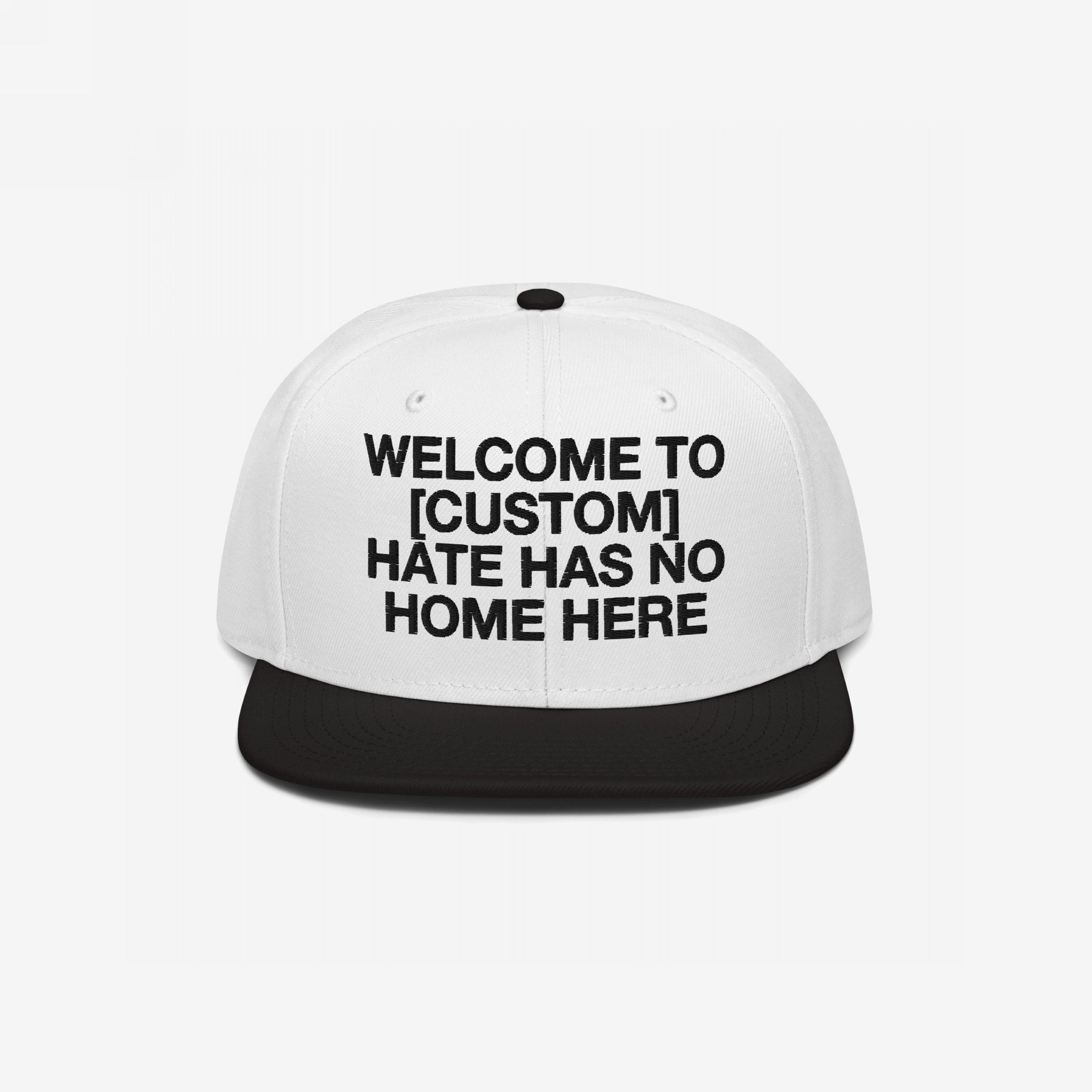 Custom Hate Has No Home Here Snapback Hat with a white crown and black brim, featuring bold black text for personalizing your city name. Embroidered EGOPROOF logo on the back, emphasizing unity and justice.