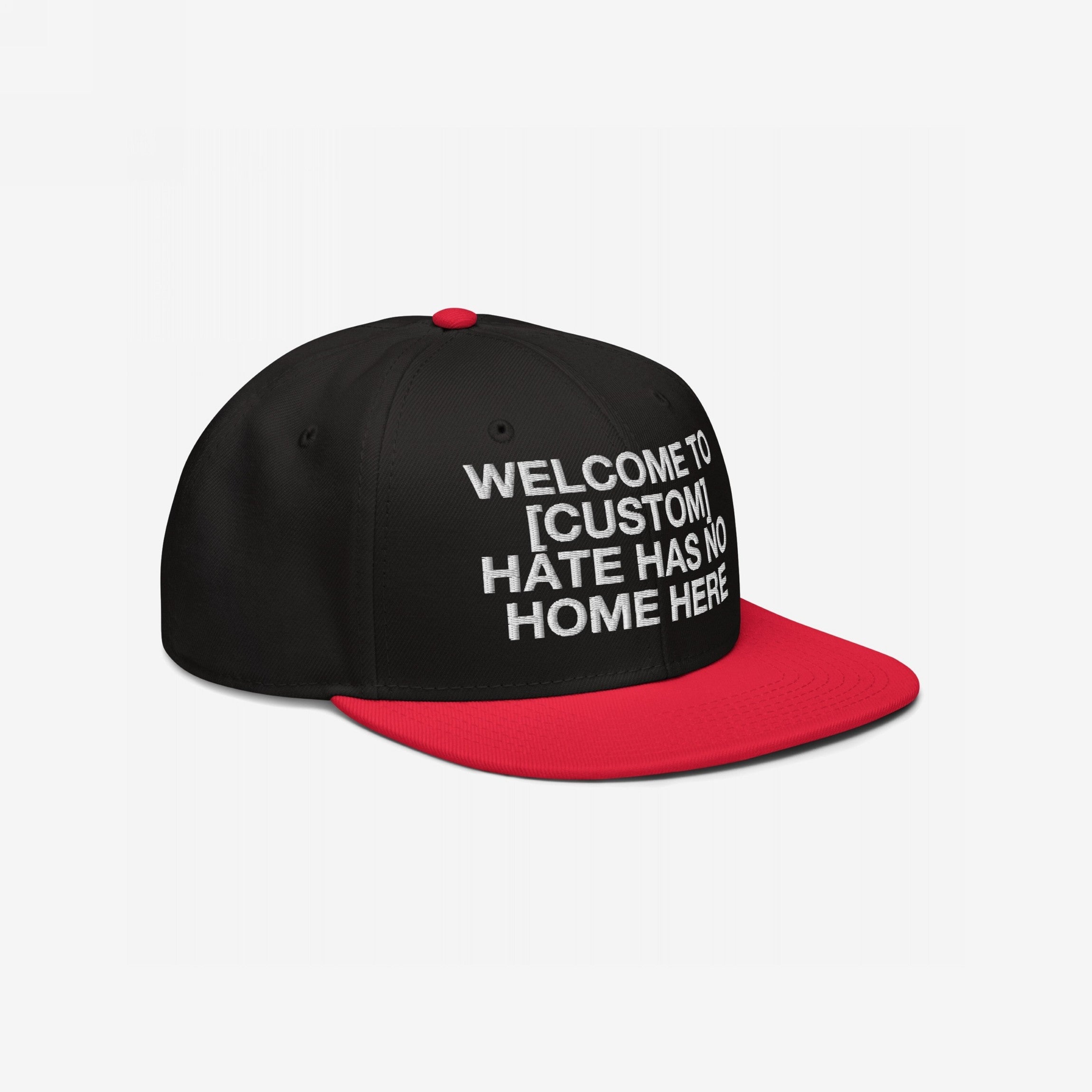Custom Hate Has No Home Here Snapback Hat featuring a black crown and bright red flat brim with bold white embroidery. The message is customizable to include your city, promoting justice and unity.