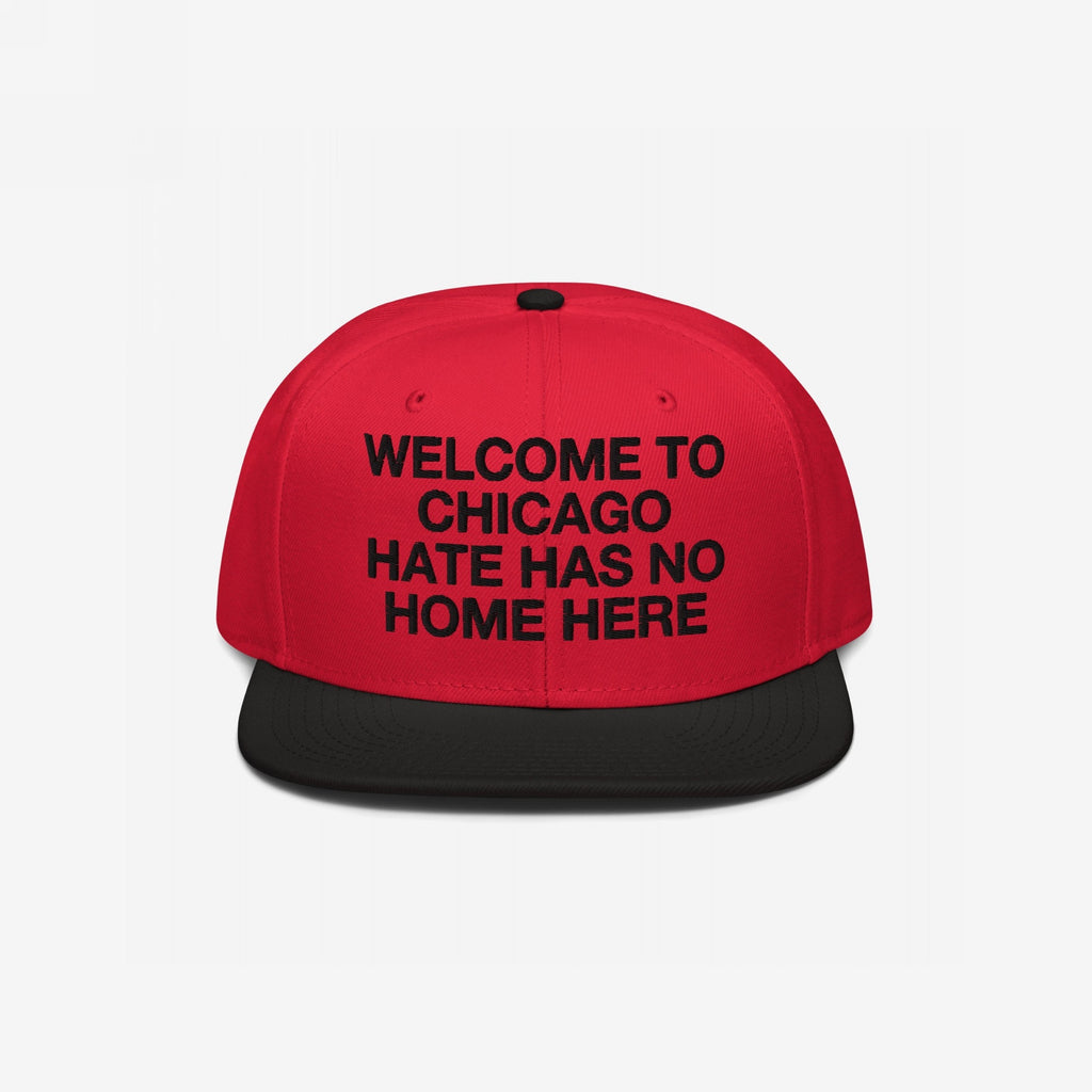 Custom Hate Has No Home Here Snapback Hat features a red crown and black visor, with an impactful slogan embroidered on the front. Highlights activism with adjustable snap closure and urban style.