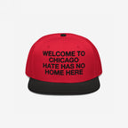 Custom Hate Has No Home Here Snapback Hat features a red crown and black visor, with an impactful slogan embroidered on the front. Highlights activism with adjustable snap closure and urban style.