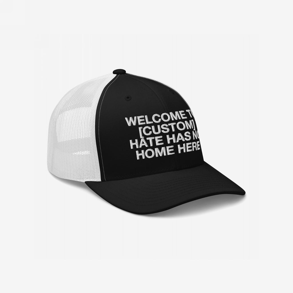 Custom Hate Has No Home Here Trucker Hat features bold embroidery: WELCOME TO [CUSTOM] HATE HAS NO HOME HERE, on a structured front with a breathable mesh back, promoting unity and equality.