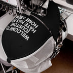 Custom Hate Has No Home Here Trucker Hat on embroidery machine, stitching “WELCOME TO [YOUR CITY]: HATE HAS NO HOME HERE.” Features structured front, breathable mesh back, adjustable snapback for personalization.
