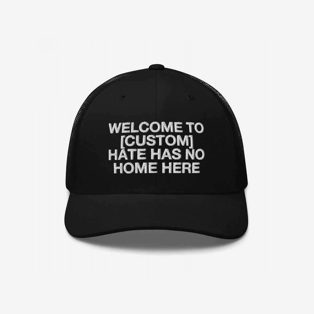 Custom Hate Has No Home Here Trucker Hat featuring white embroidered text, structured front, and mesh back. This adjustable cap promotes unity and inclusivity with a personalized city message.