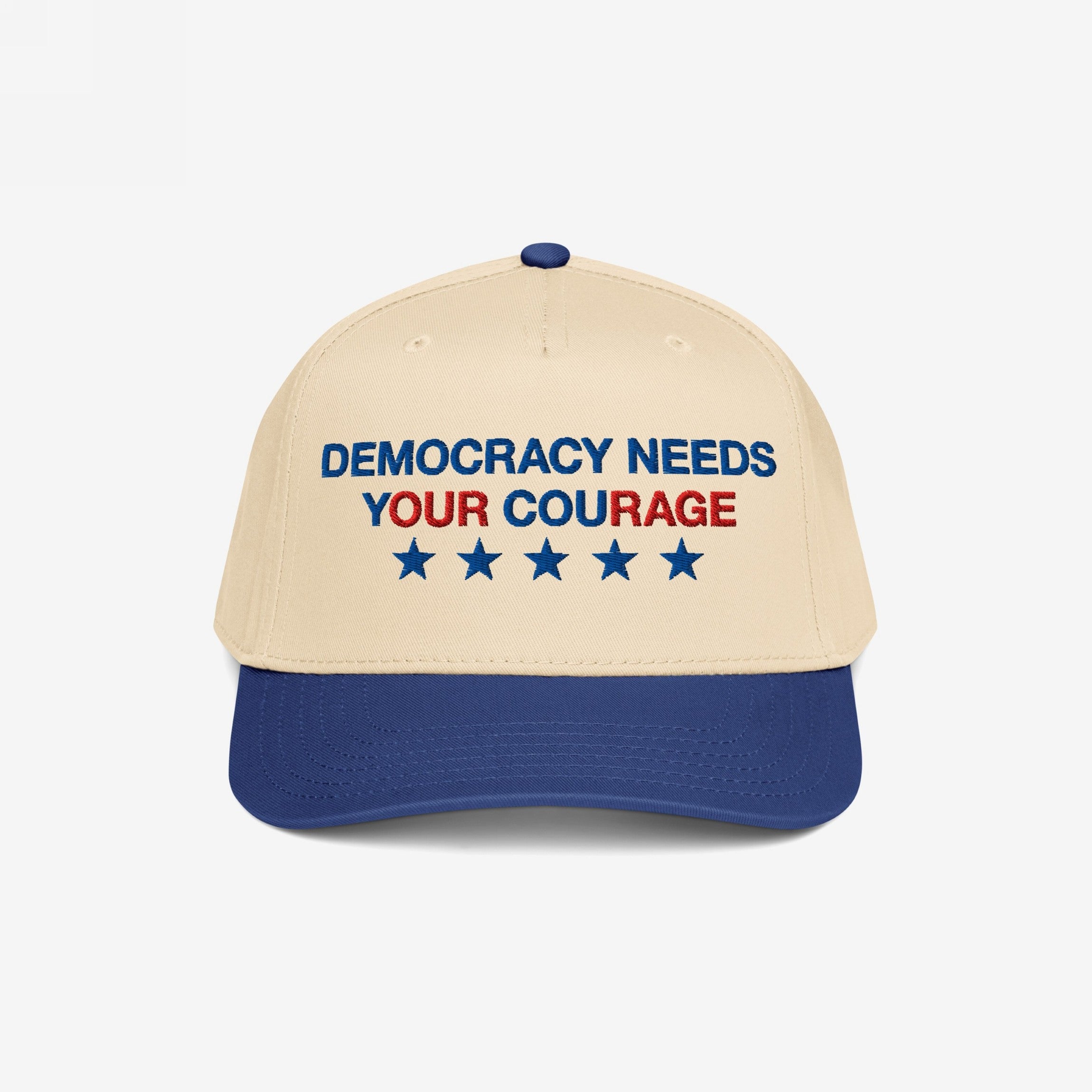 Two-tone Democracy Hat with beige front, blue bill. Embroidered “DEMOCRACY NEEDS YOUR COURAGE” in blue and red, with five stars. A bold statement accessory aligned with equality and anti-fascist values.