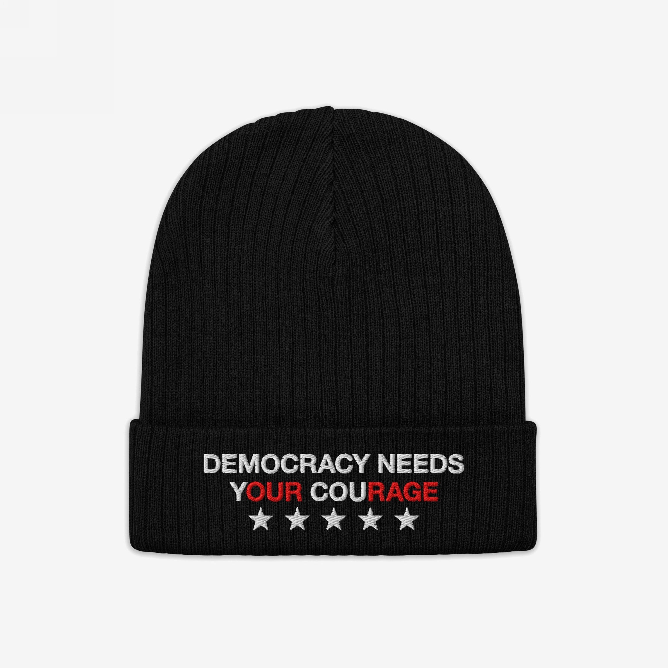 The Democracy Hat is a black knit beanie with a folded cuff, featuring the embroidered slogan DEMOCRACY NEEDS YOUR COURAGE in white and red, accented by five white stars.