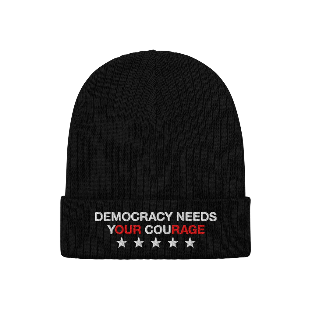 The Democracy Hat is a black knit beanie with a folded cuff, featuring the embroidered slogan DEMOCRACY NEEDS YOUR COURAGE in