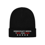 The Democracy Hat is a black knit beanie with a folded cuff, featuring the embroidered slogan DEMOCRACY NEEDS YOUR COURAGE in