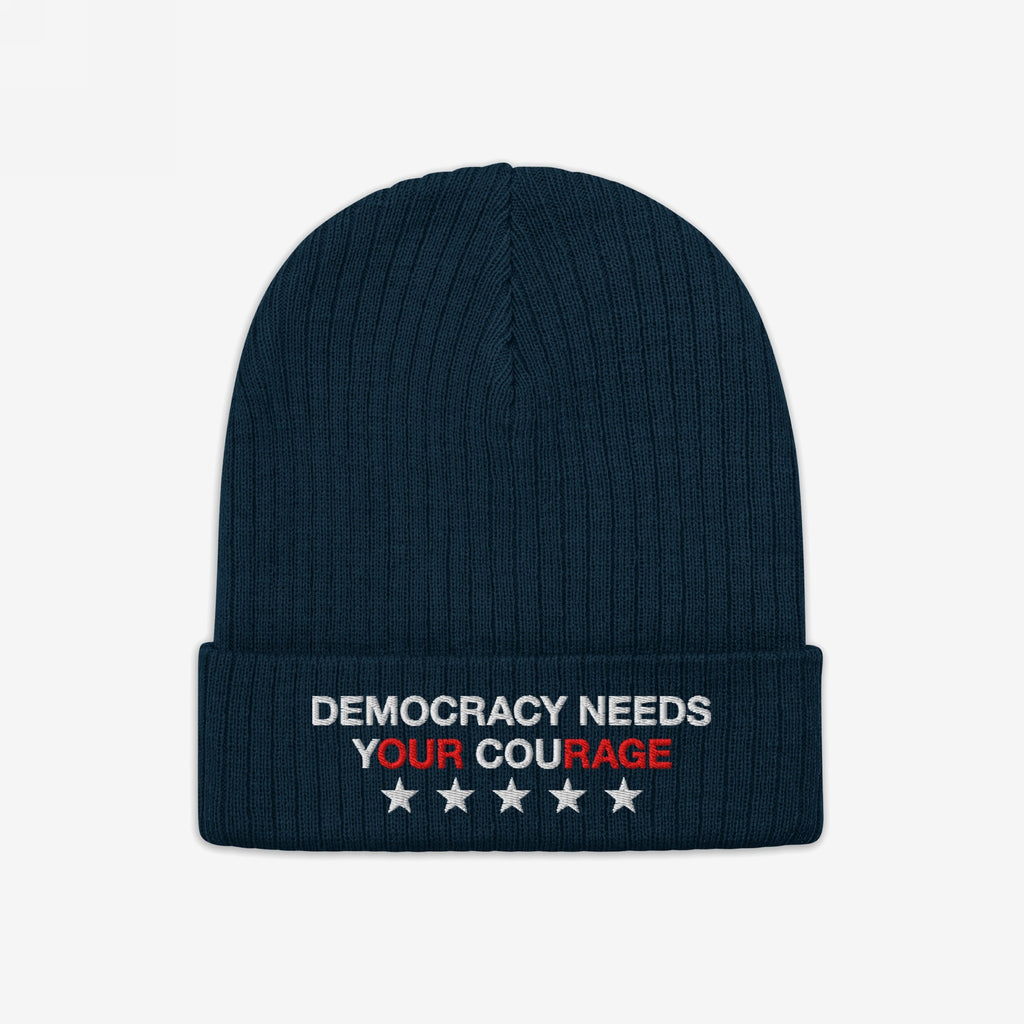Democracy Hat: A dark-navy ribbed knit beanie featuring “DEMOCRACY NEEDS YOUR COURAGE” embroidered on the cuff, emphasizing Our Rage, with five white stars, embodying anti-fascist and equality values.