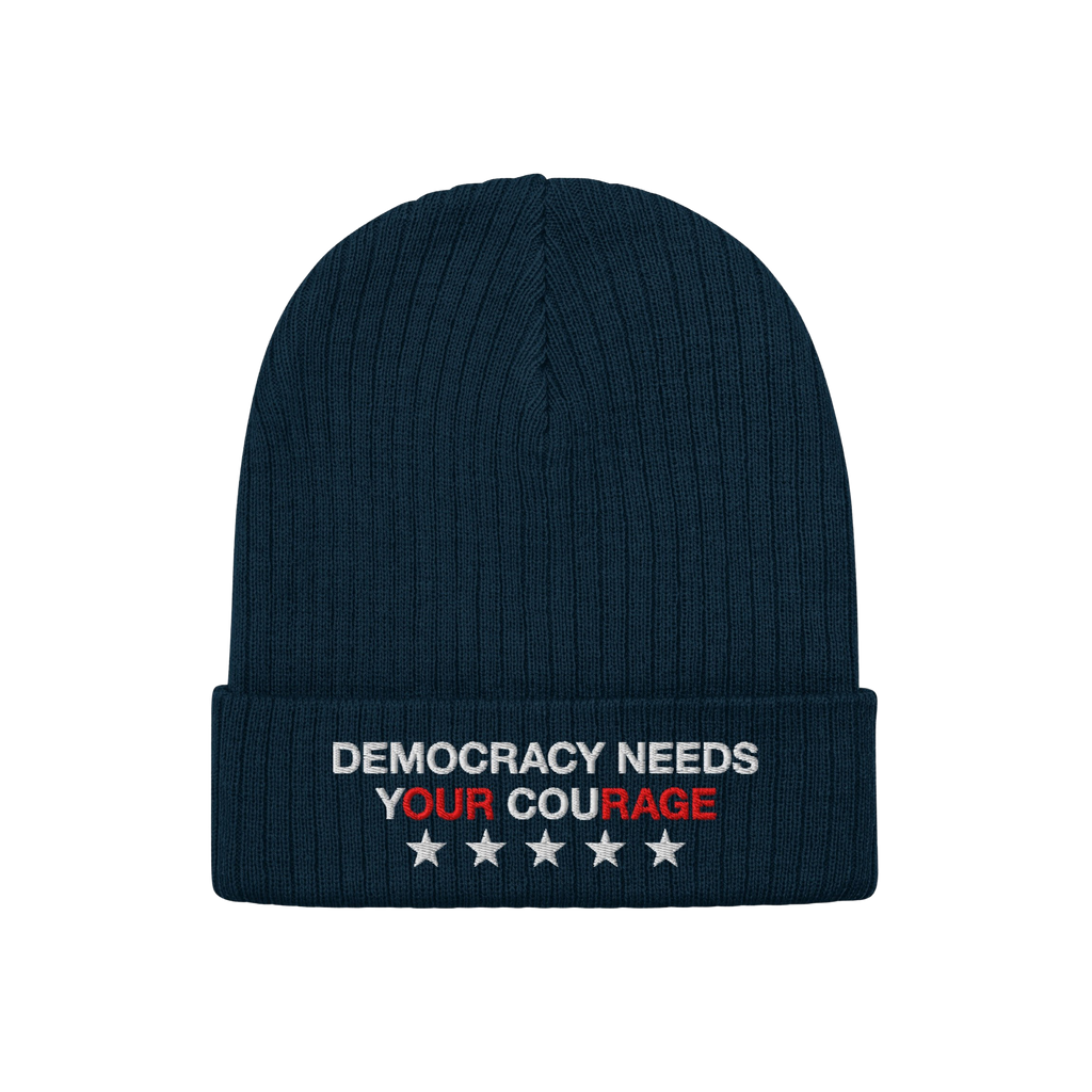 Democracy Hat: A dark-navy ribbed knit beanie featuring “DEMOCRACY NEEDS YOUR COURAGE” embroidered on the cuff, emphasizi