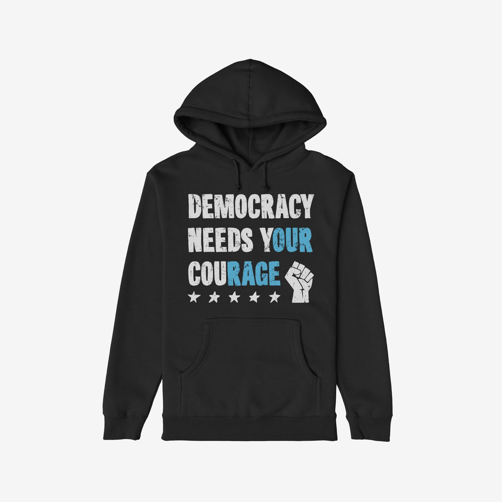 Black pullover hoodie titled Democracy Shirt, featuring the slogan “DEMOCRACY NEEDS YOUR COURAGE” in distressed white and blue type with a white raised-fist graphic and stars, embodying bold protest energy.
