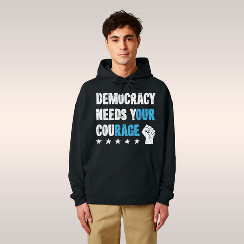 Two young adults showcase the Democracy Shirt, featuring the bold slogan “Democracy Needs Your Courage.” Each hoodie disp