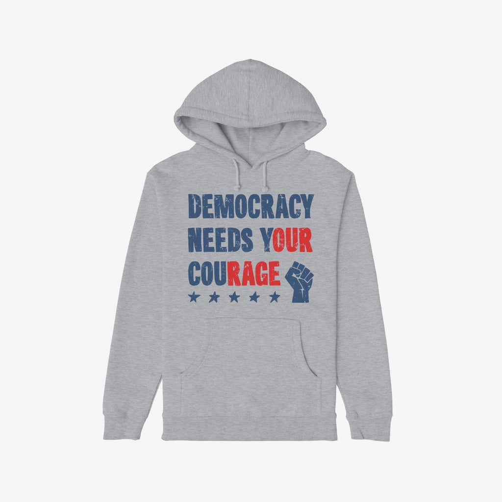 Democracy Shirt: Light-gray hoodie with stencil-style DEMOCRACY NEEDS YOUR COURAGE graphic, featuring distressed stars and raised-fist icon, symbolizing protest energy and resilience. Available in various styles.