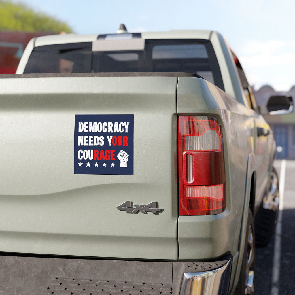 A light-green pickup truck displays the Democracy Sticker & Magnet on its tailgate, featuring DEMOCRACY NEEDS YOUR COURAGE with a raised fist icon, urging action against authoritarianism and supporting progressive voices.