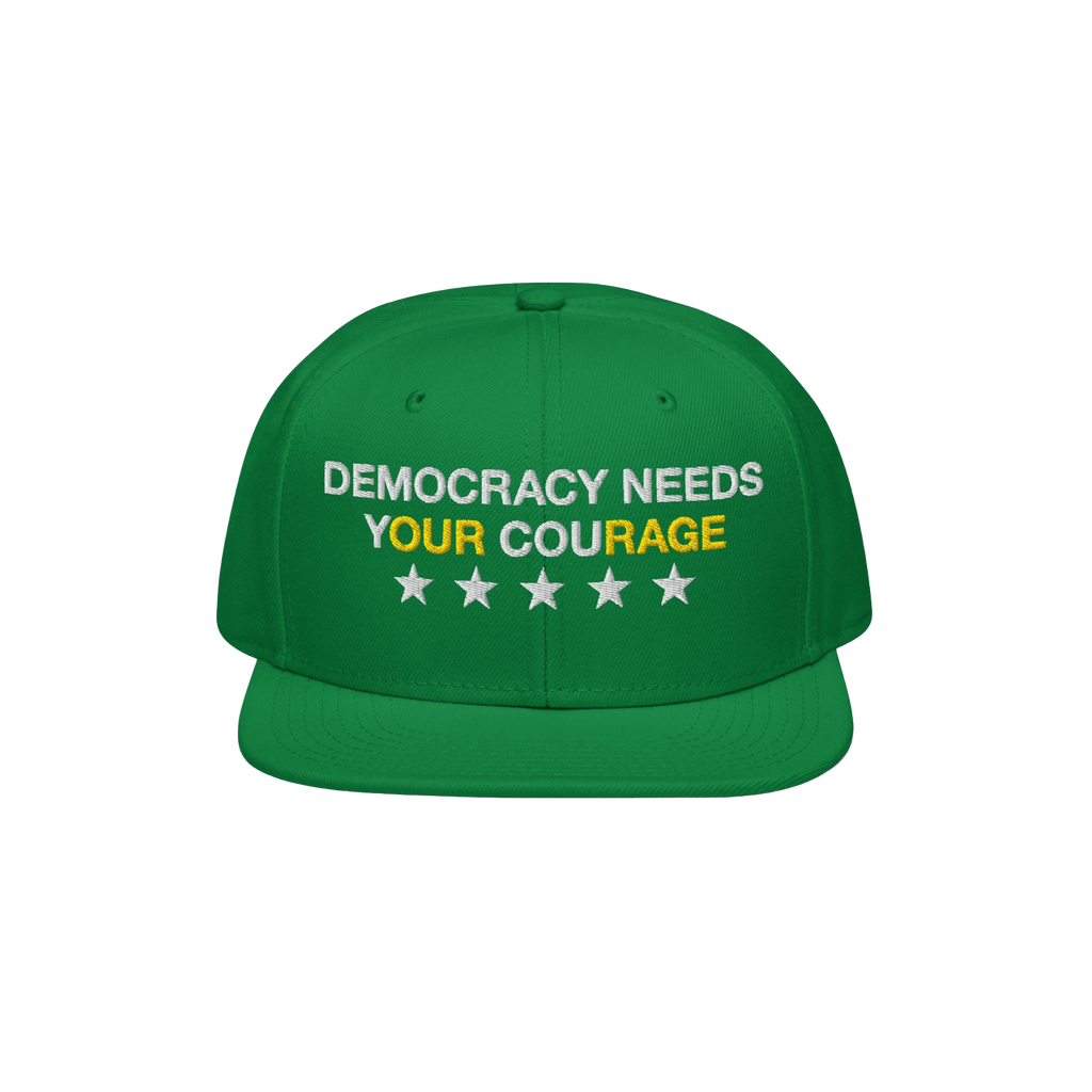 Green Democracy Hat with block letters “DEMOCRACY NEEDS YOUR COURAGE,” highlighting “YOUR COURAGE” in yellow. Feature