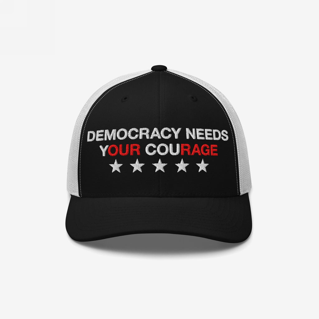 Democracy Hat with the slogan DEMOCRACY NEEDS YOUR COURAGE embroidered on the front, featuring emphasized red lettering YOUR and RAGE, and a row of stars, reflecting bold, anti-fascist values.