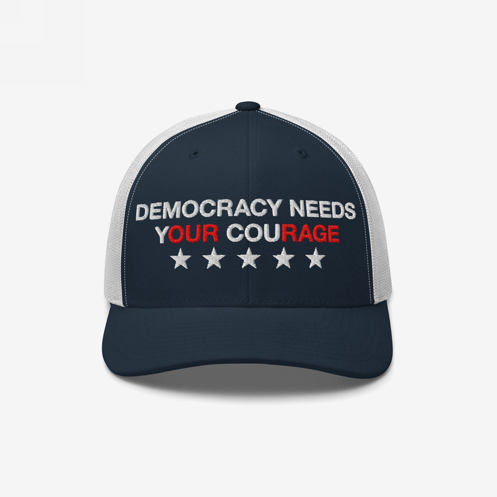Democracy Hat featuring DEMOCRACY NEEDS YOUR COURAGE slogan with red-highlighted words, embroidered on navy-blue and white mesh trucker cap, adorned with five stars for an empowering statement.