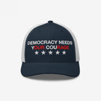 Democracy Hat featuring DEMOCRACY NEEDS YOUR COURAGE slogan with red-highlighted words, embroidered on navy-blue and white mesh trucker cap, adorned with five stars for an empowering statement.
