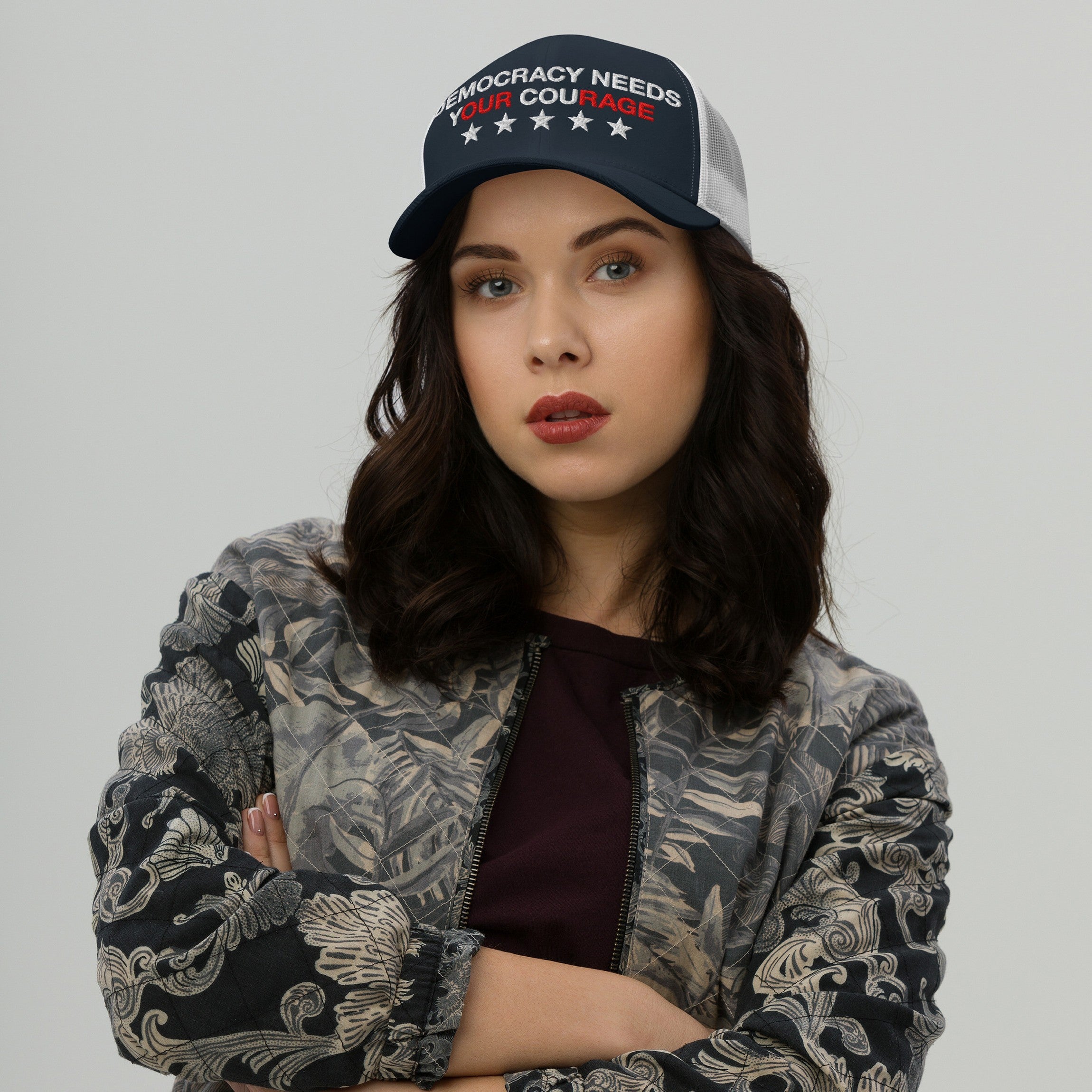 Young woman wearing a Democracy Hat with “Democracy Needs Your Courage” embroidered, posing confidently. The hat emphasizes activism and protest, aligning with anti-fascist values and support for equality.