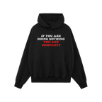 Don't Be Complicit Hoodie, black with kangaroo pocket and drawstring hood, features bold slogan IF YOU ARE DOING NOTHING, YOU