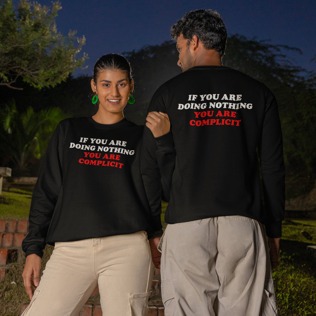 Two people outdoors wearing Don't Be Complicit Hoodie & Sweatshirt. The woman faces forward smiling, while the man shows the slogan on his back, embodying active resistance and awareness.